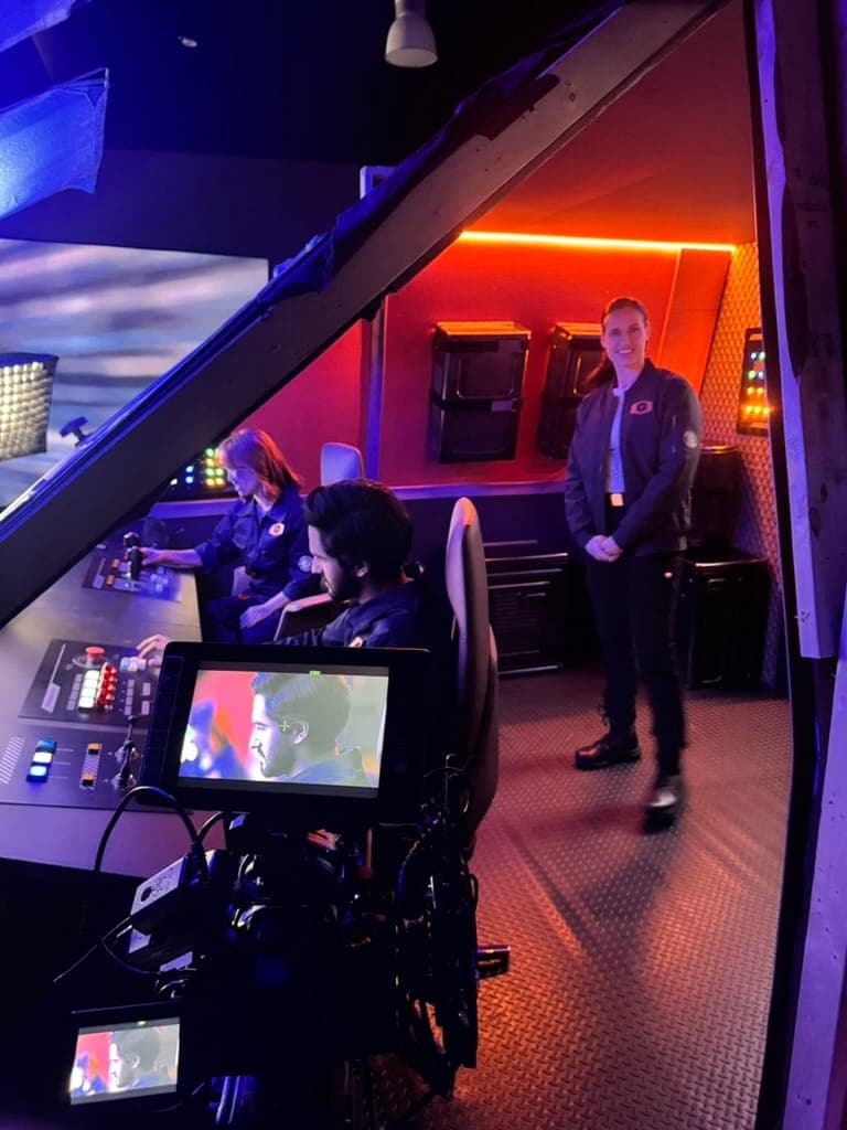 The camera rolling on actors in flight suits at the cockpit controls